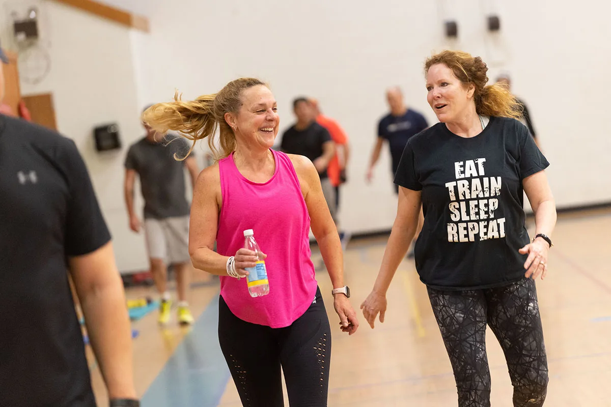 Two women leave fitness class smiling and talking as they rehydrate