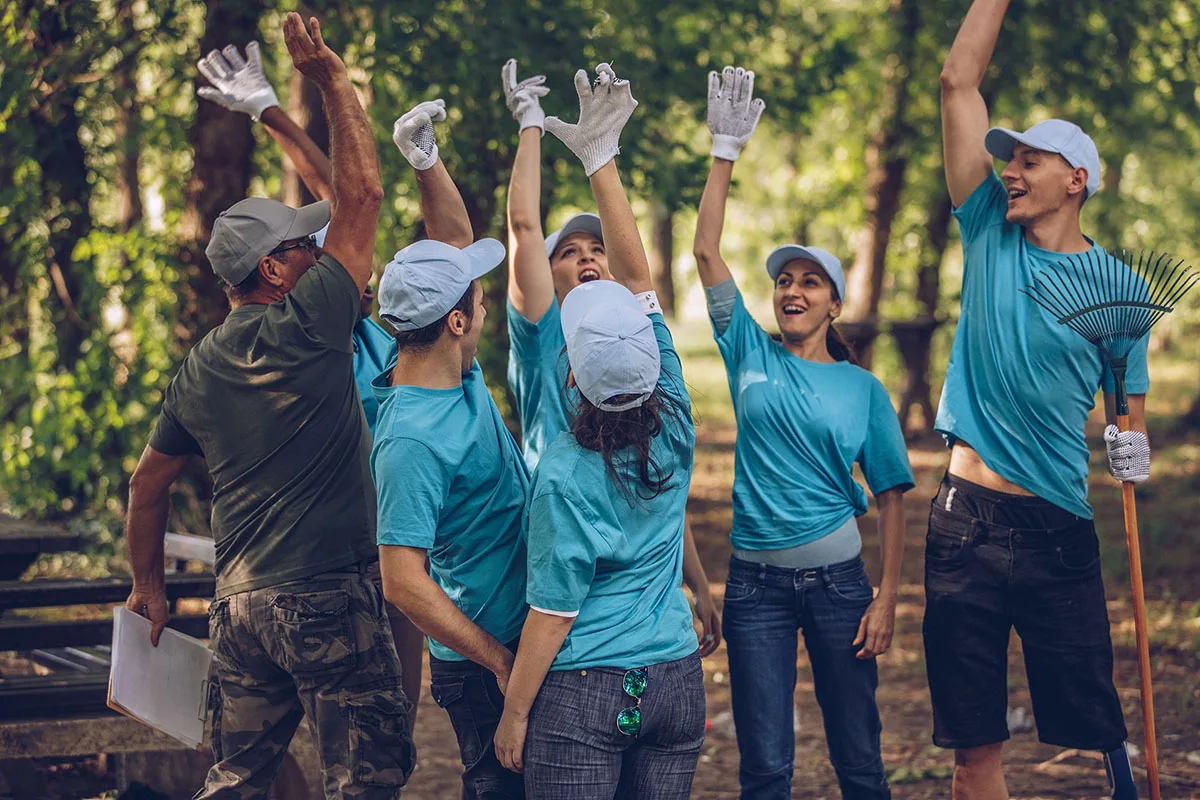 A community volunteer group from the Valley Shore YMCA raise their hands in the air, work gloves on, to celebrate supporting the community.